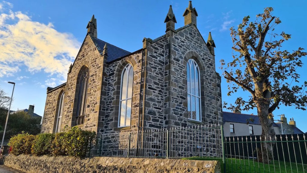 Stone church building with pointed gables, pinnacles and tall arched windows behind green railings