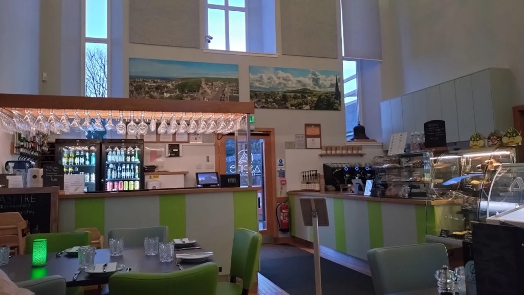 Striped green and white bar and counter with hanging glasses, drinks fridges, coffee machine and a cake cabinet