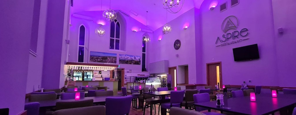 Restaurant hall lit in purple with chandeliers, arched windows and an Aspire Restaurant sign on the wall