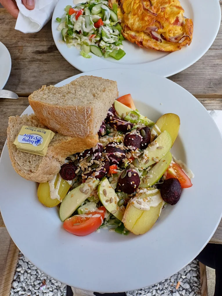Salad with beetroot, apple, potato, tomato and seeds, served with bread and butter, beside an omelette and coleslaw