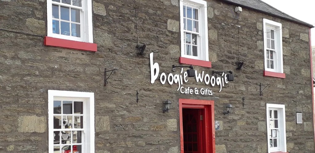 Stone frontage with red-framed door and windows and a white sign reading Boogie Woogie Cafe and Gifts