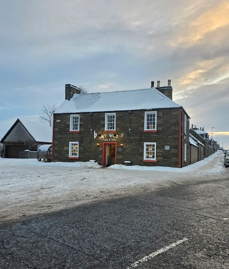 Stone building with red door and window trims, signed Boogie Woogie Cafe and Gifts, with snow on the roof and road