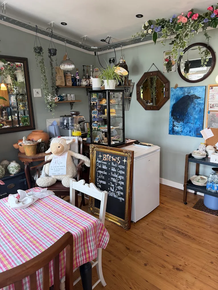 Café corner with a chalkboard drinks menu, cake cabinet, mirrors, hanging plants and a gingham-covered table