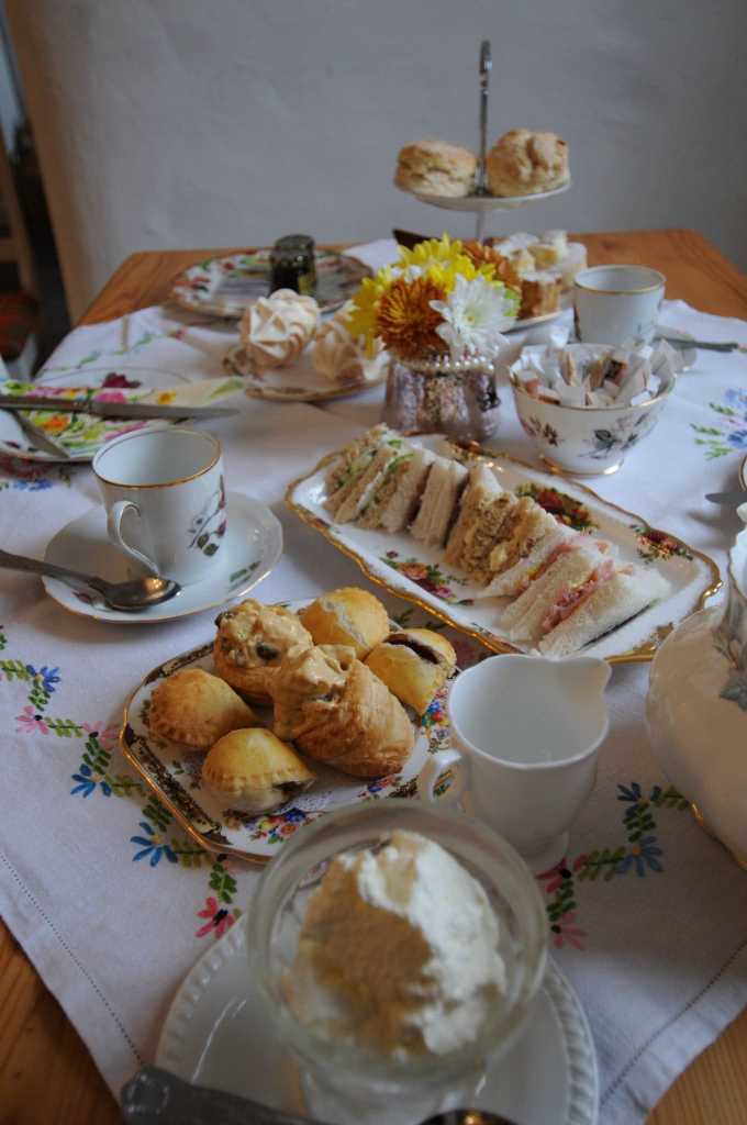 Afternoon tea on an embroidered tablecloth with sandwiches, pastries, scones on a stand, meringues, flowers and china cups