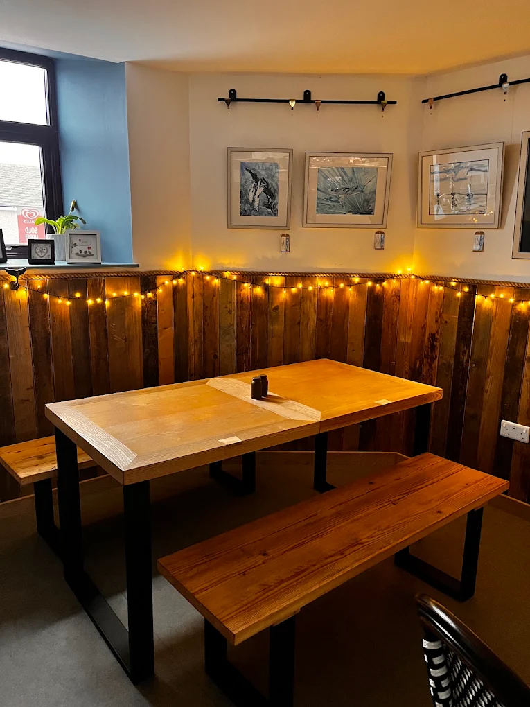 Wooden table and benches in a corner with wood panelling, fairy lights and framed drawings on the wall