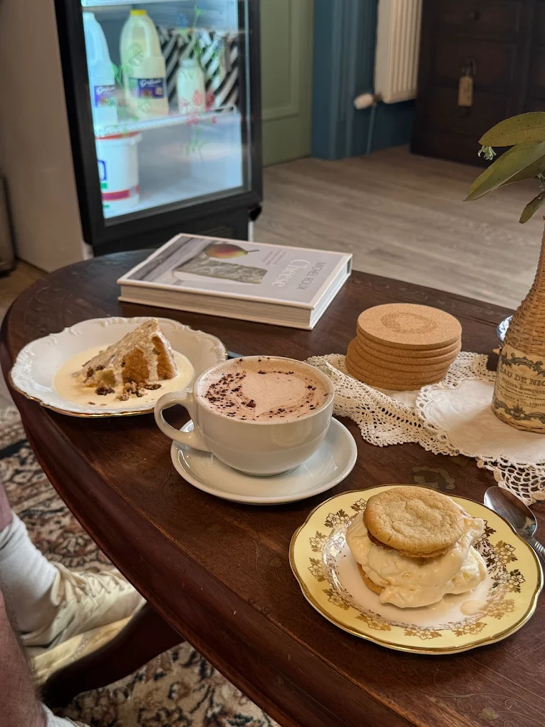 Wooden table with a hot chocolate, a slice of cake with custard and a cookie ice cream sandwich on vintage plates