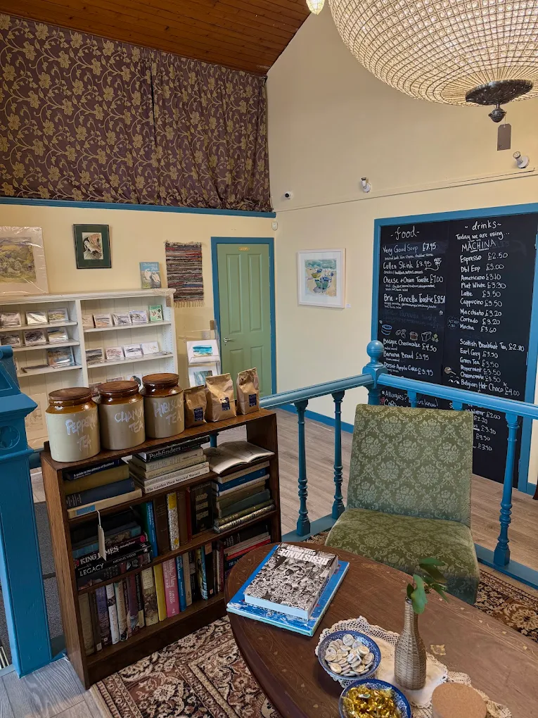 Cafe mezzanine with a chalkboard food and drinks menu, bookshelf, tea jars, green armchair and wooden table