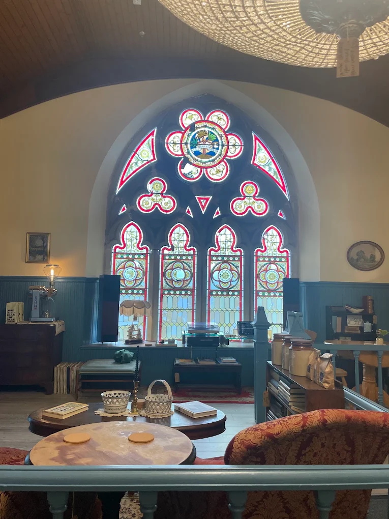 Cafe interior with a large red and yellow stained glass window, armchairs, round tables and a crystal chandelier