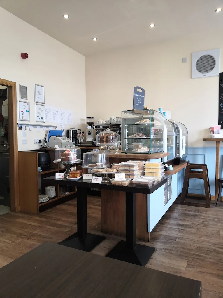 Café counter with cakes under glass domes, a display cabinet, coffee machine and a table of packaged treats